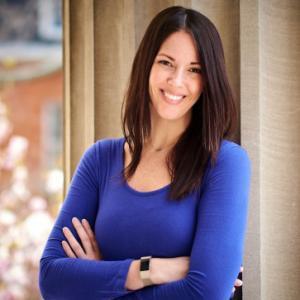 Photo of Emily-Anne McCormack. She is standing outside. She is smiling and has her arms folded across her chest. She is wearing a blue sweater and a watch.