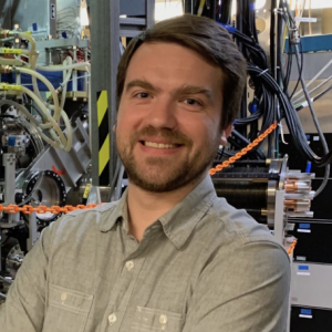 Photo of a young white man standing in front of lab equipment
