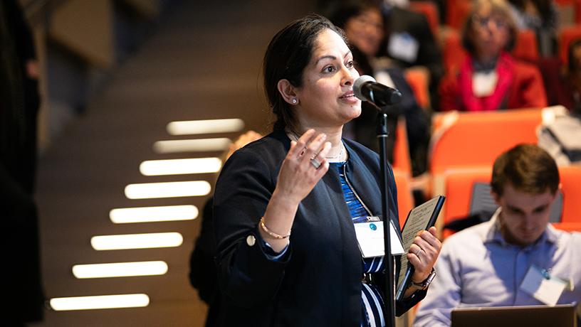 A female audience member speaking into a microphone. Other audience members sit in the background