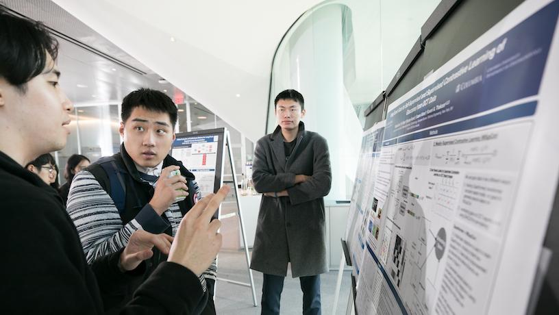 Three symposium attendees gesturing to a research poster in front of them.