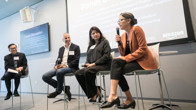 Four panelists sit in their chairs on stage. The panelist furthest to the right speaks into the microphone.