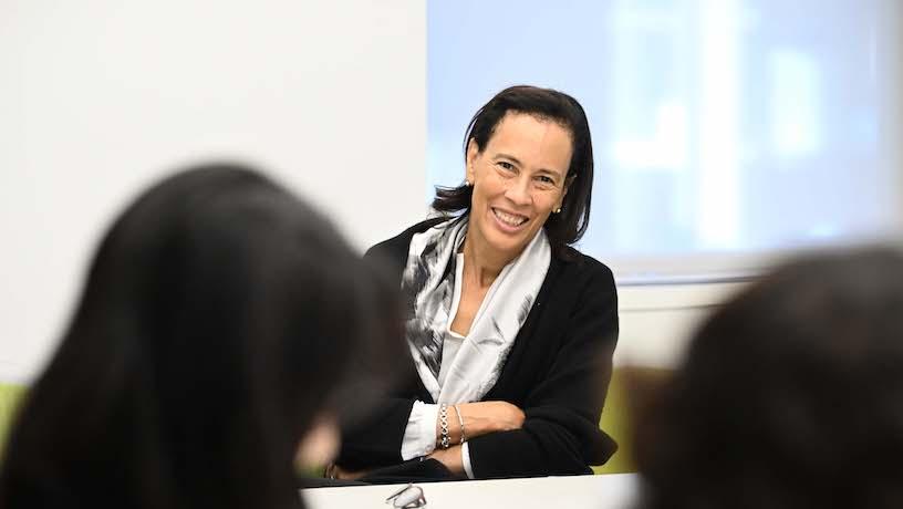 A smiling Anne Gates sitting at a table with her arms crossed.