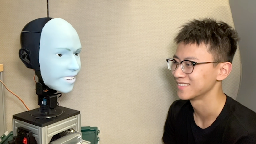 A robotic face and a person smiling at each other