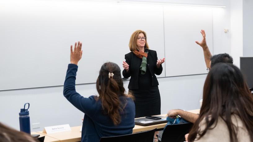 Georgia Papathomas standing in front of the room with students raising their hands