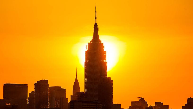 The Empire State building blocks the low Sun. The sky is orange