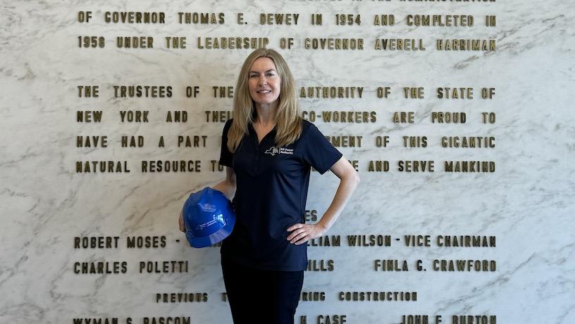 Alexis Harley holding a hard hat and posing for a photo in front of a plaque