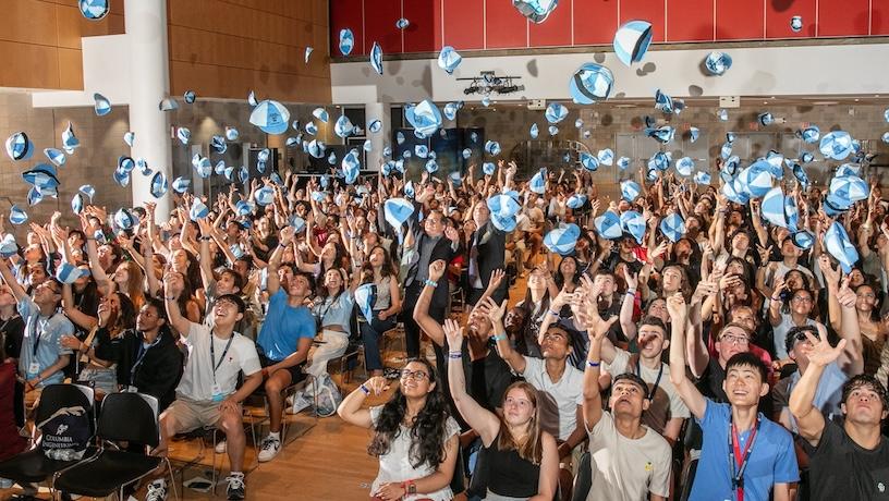 Countless Columbia Engineering incoming students sitting in an auditorium and throwing beanies in the air